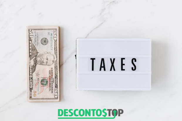 pilha de notas de dólares ao lado de uma placa onde está escrito taxes